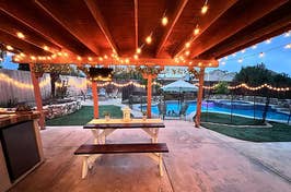 Backyard patio with string lights, picnic table, and pool view at dusk