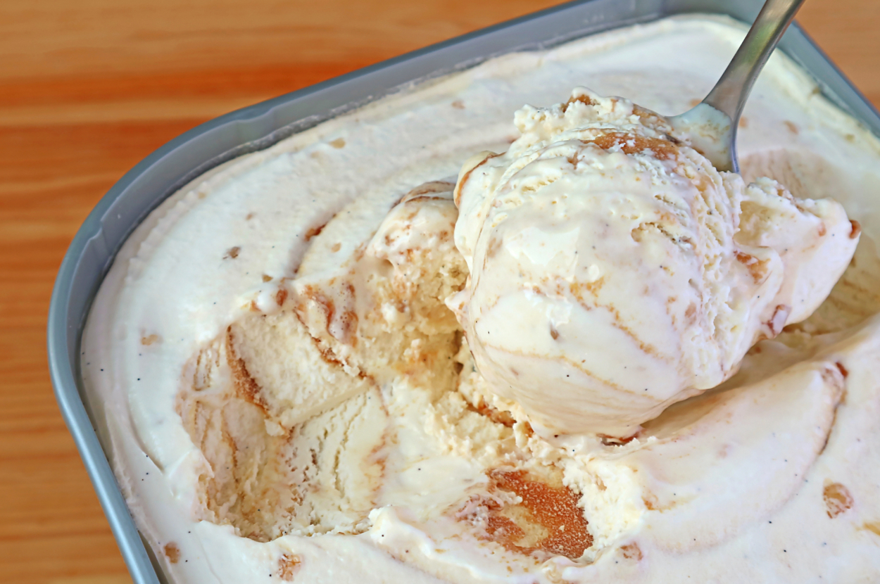 A spoon scooping vanilla ice cream with caramel swirls from a container