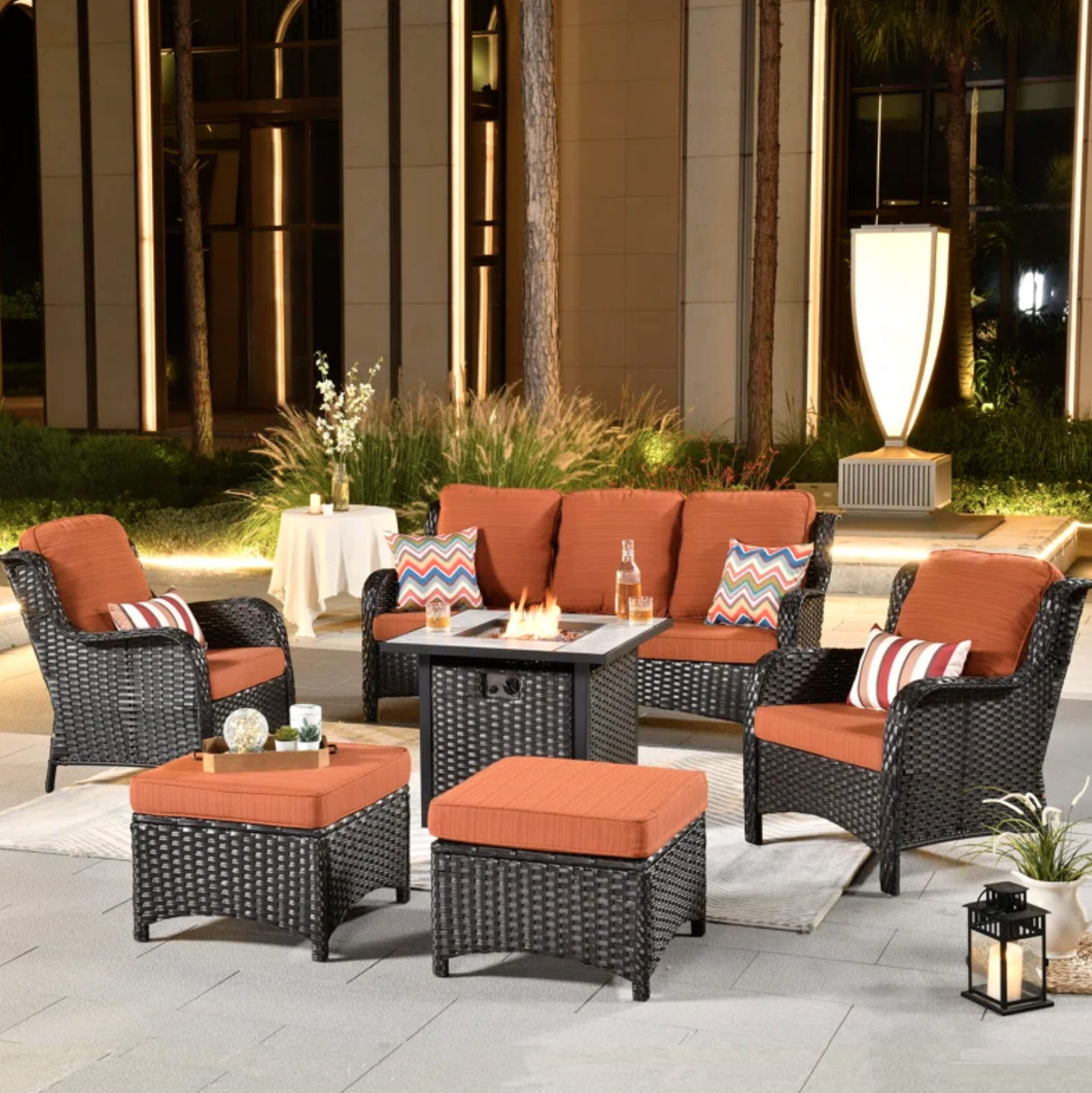 Outdoor furniture set with a fire pit table, two armchairs, a sofa, and decorative orange cushions