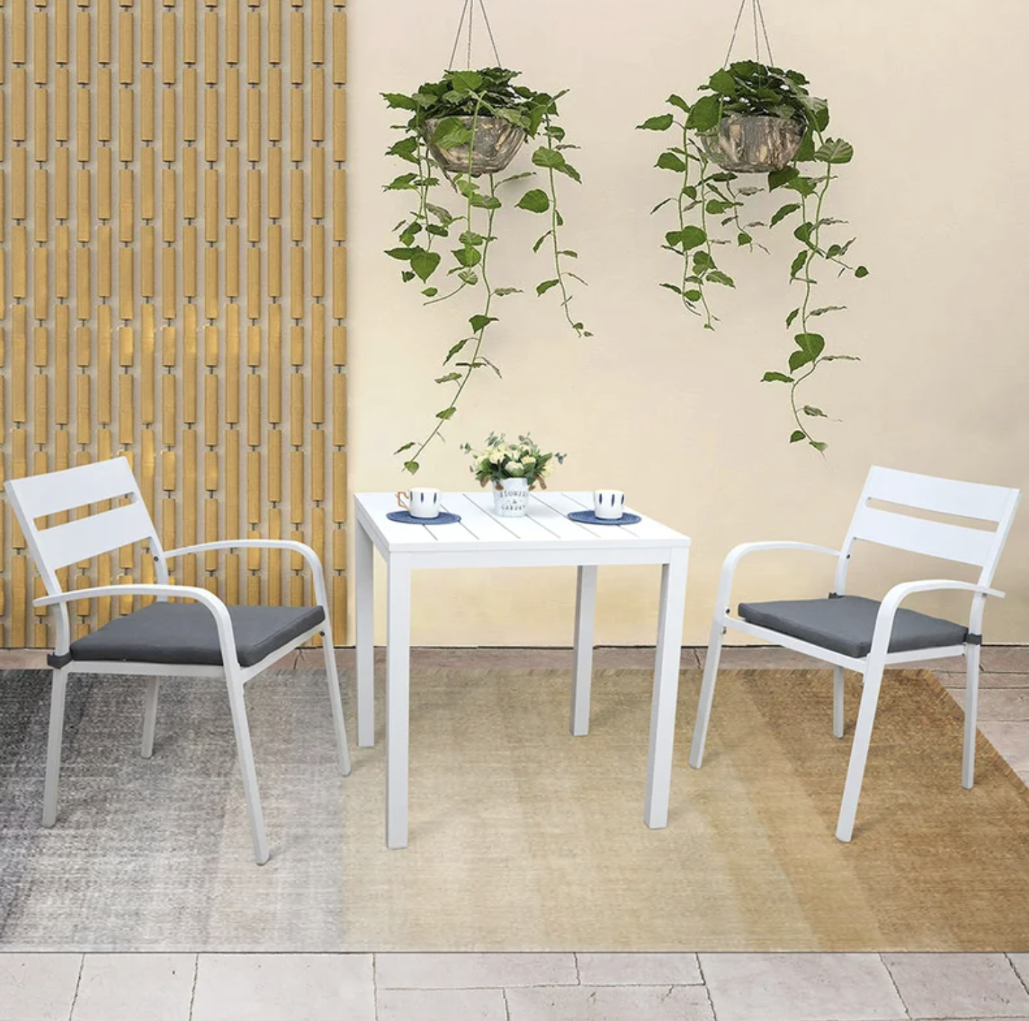Patio furniture set with a white table and two chairs, placed against a neutral wall with hanging planters