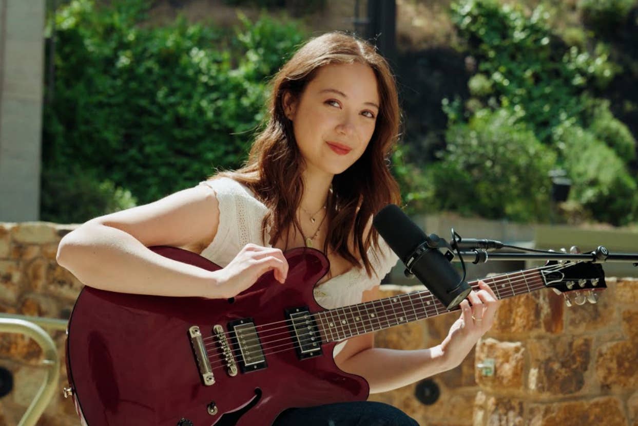 Woman sitting with a guitar, smiling, near a microphone, outdoors