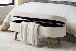 Storage bench at foot of bed, lid open displaying compartment, with a fringed throw blanket draped over one side