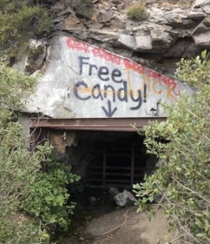 Graffiti on a rock above a small cave entrance reads &quot;Free Candy&quot; with an arrow pointing down