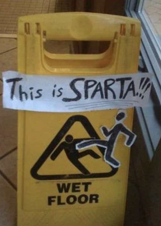 Wet floor sign with handwritten &quot;This is SPARTA!&quot; taped above the caution symbol