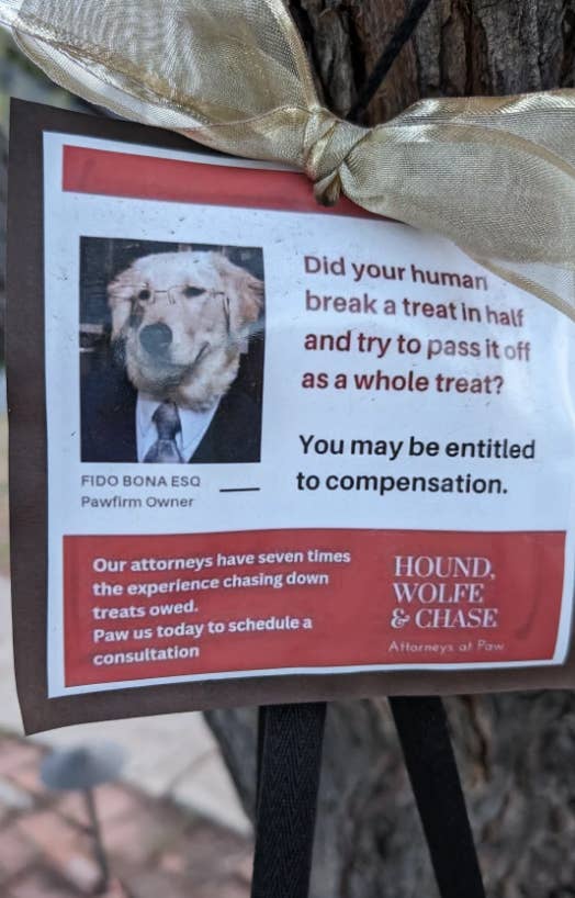 Sign about dog lawyer services with humorous text and a dog&#x27;s picture, attached to a tree