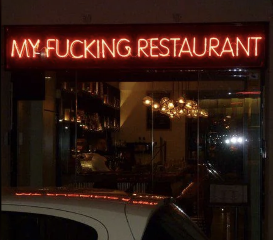 Neon sign for a provocatively named restaurant above its window front