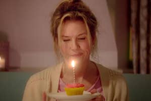 Bridget Jones with a single candle on a cupcake alone in a room.