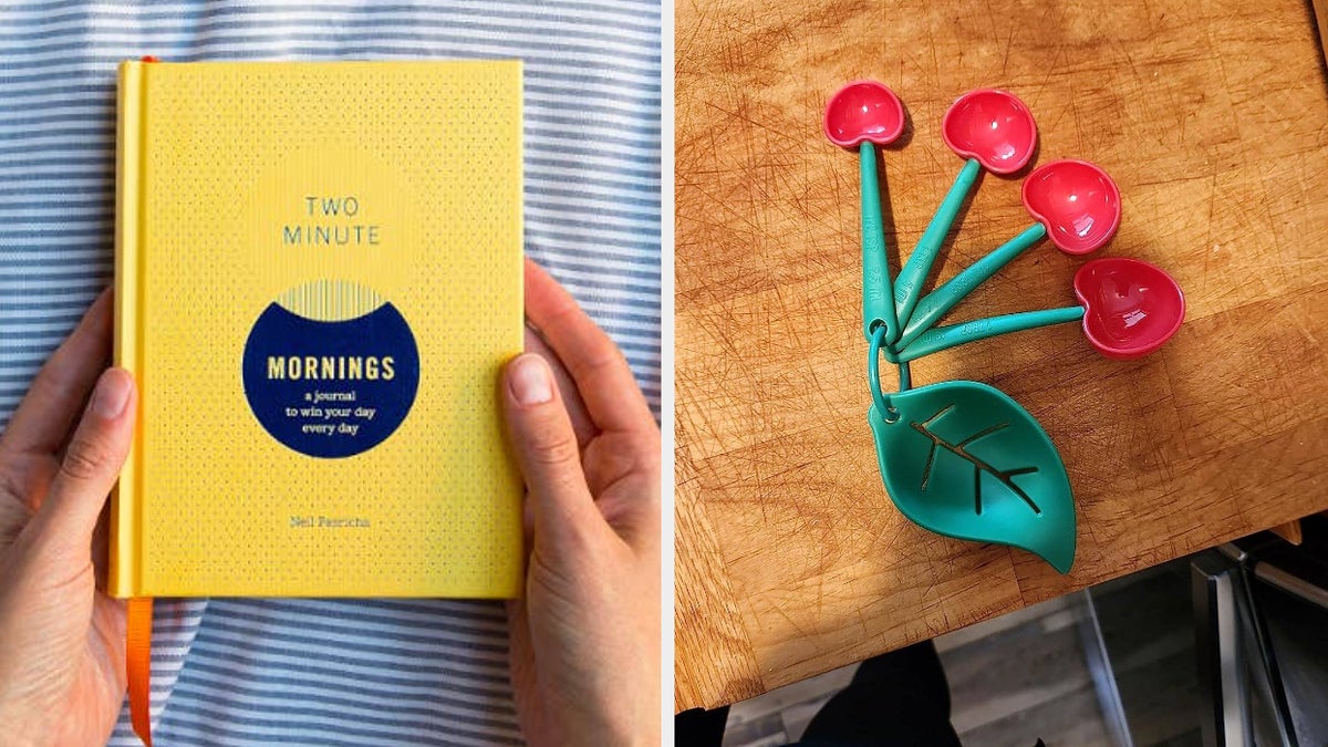 A person holds a yellow journal titled "Two Minute Mornings" next to measuring spoons shaped like cherries on a wooden surface