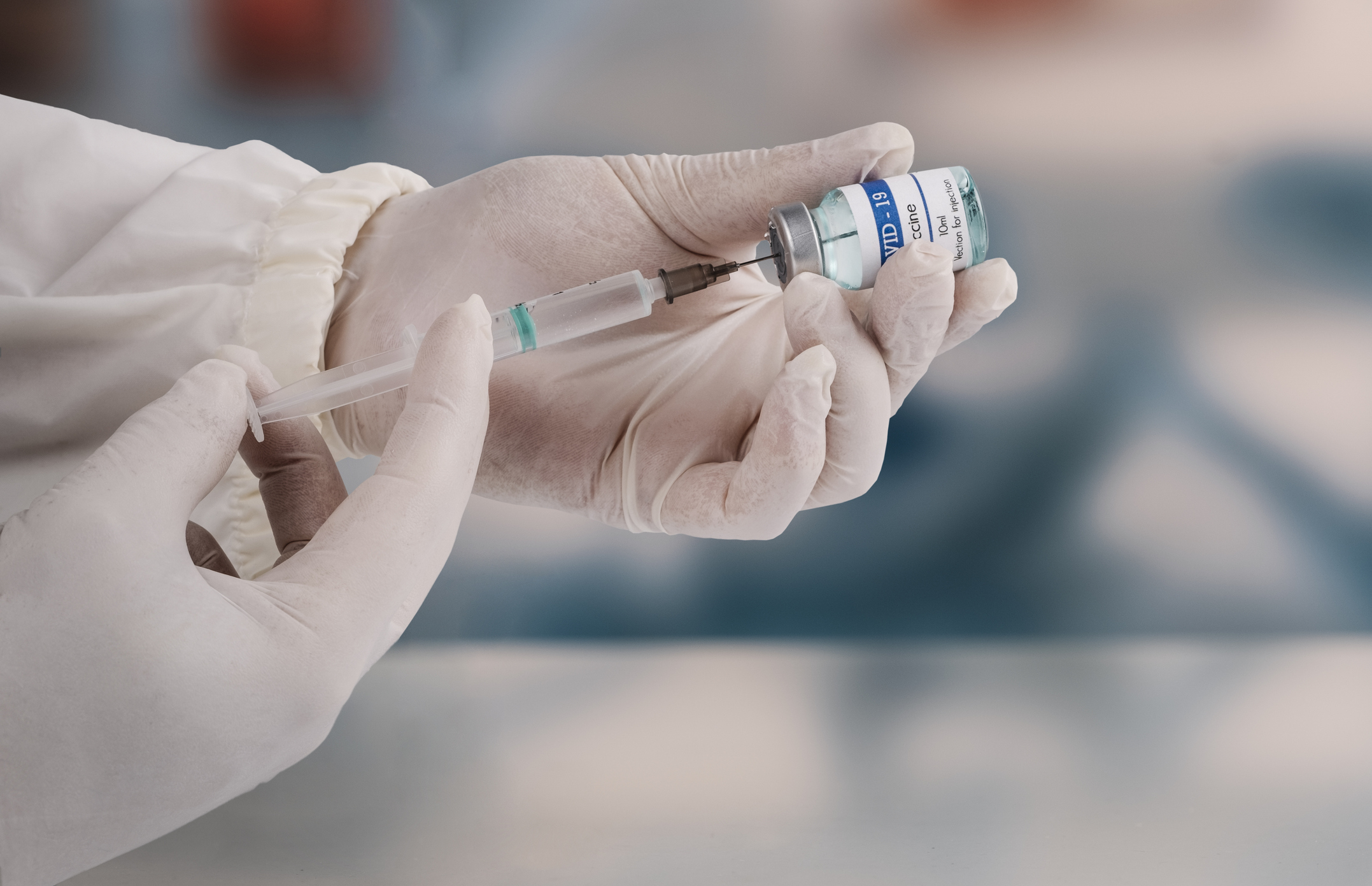 Person preparing a vaccine dose with a syringe, focused on their hands and the vial