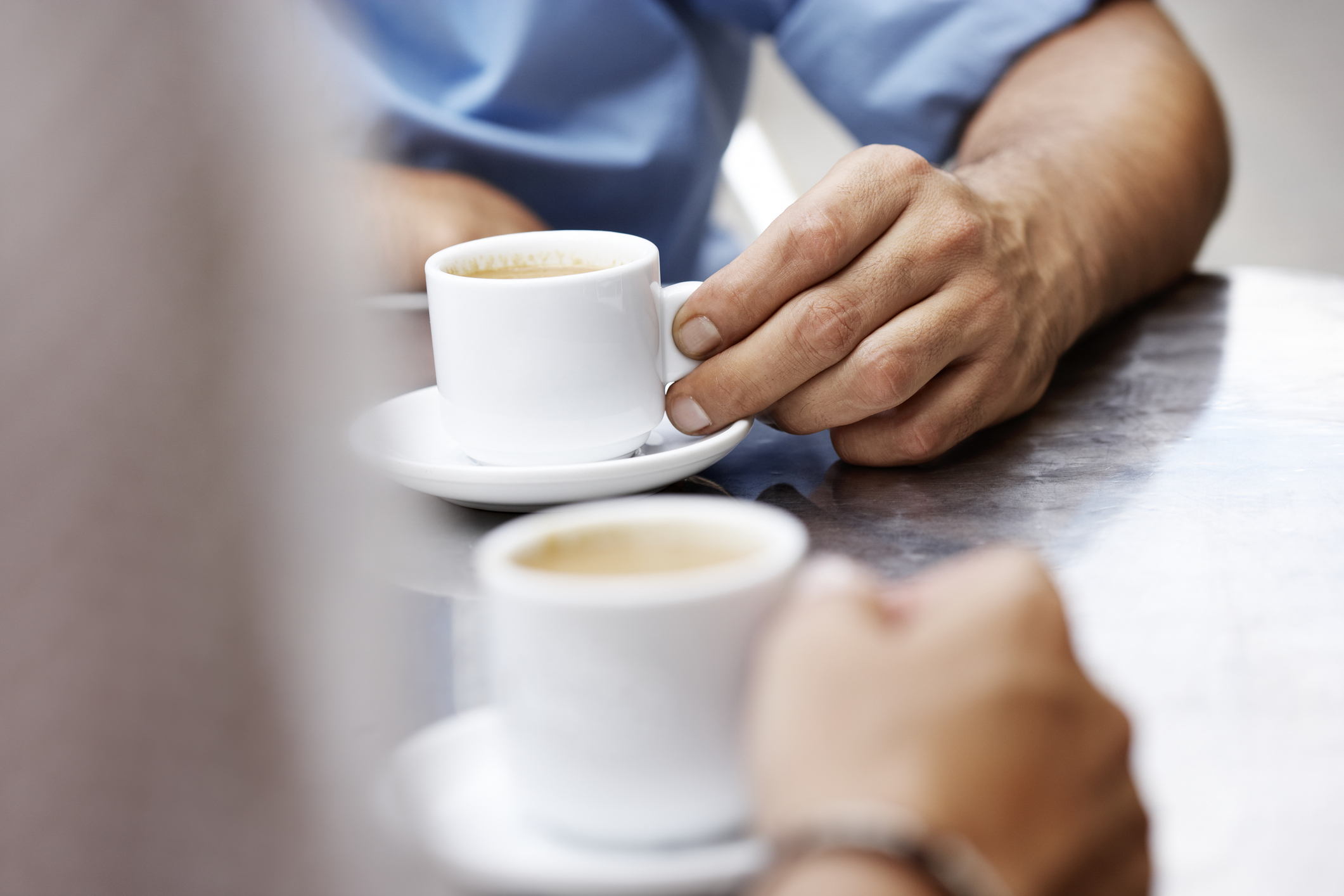 Two people at a table, one holding a small coffee cup, suggesting a casual meeting or interview