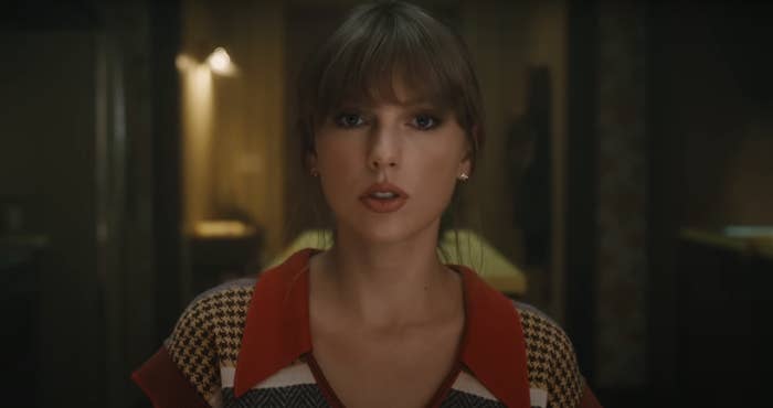 Taylor Swift in a patterned top and red cardigan, looking directly at the camera