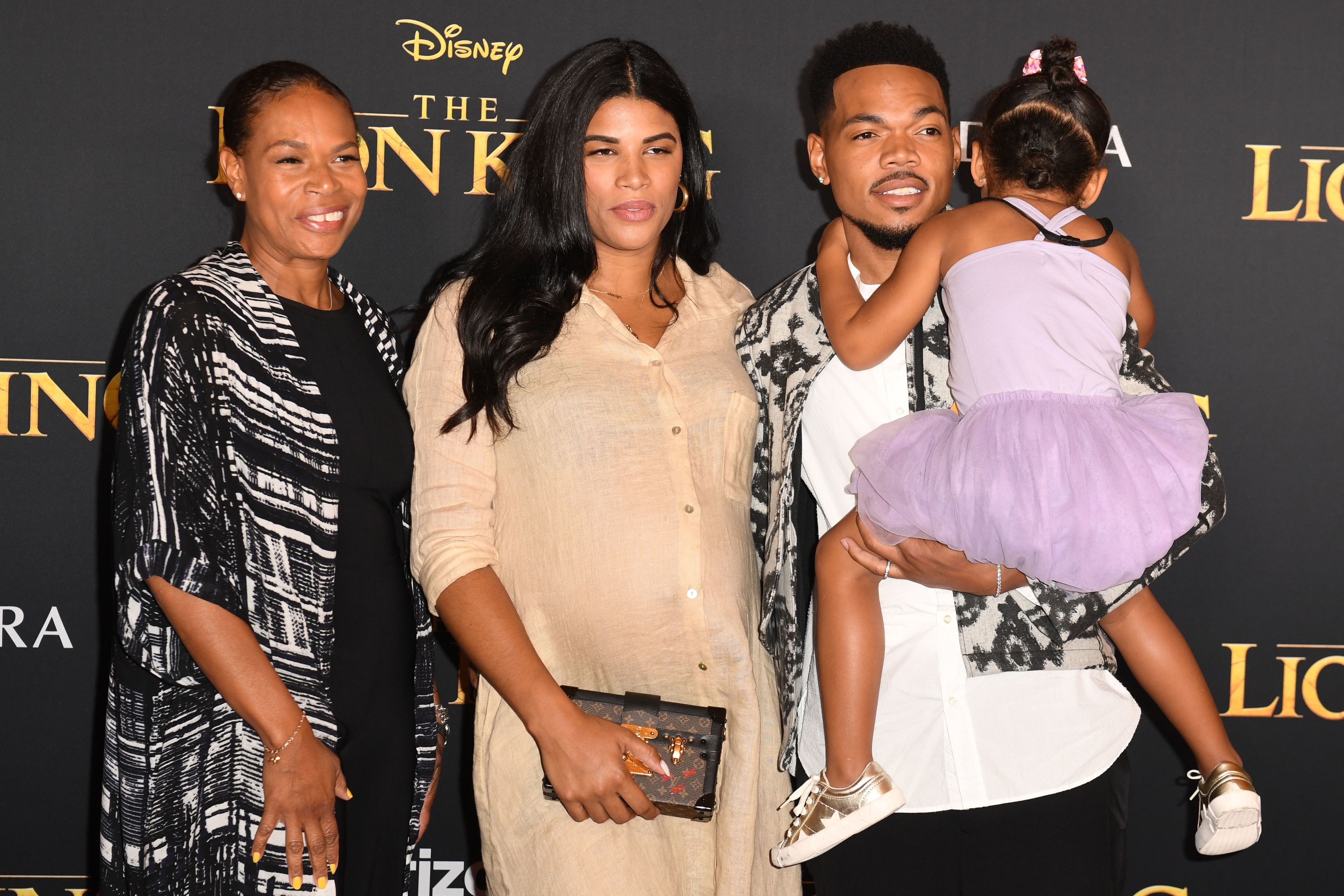 Three people at &#x27;The Lion King&#x27; premiere; a man holds a child, and two women stand beside them, dressed in smart attire