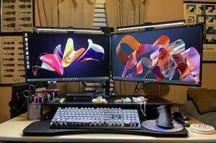 Dual computer monitors on a desk with a mechanical keyboard and various desktop accessories