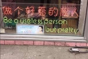 Storefront window sign says "Be a useless person but pretty" with various objects inside