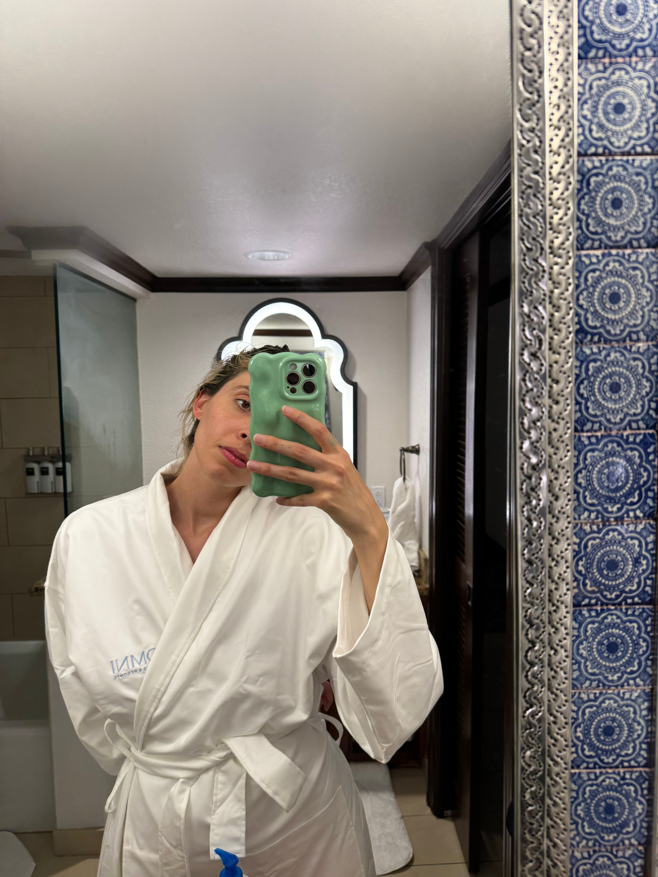 Person in a white robe taking a selfie in a bathroom mirror