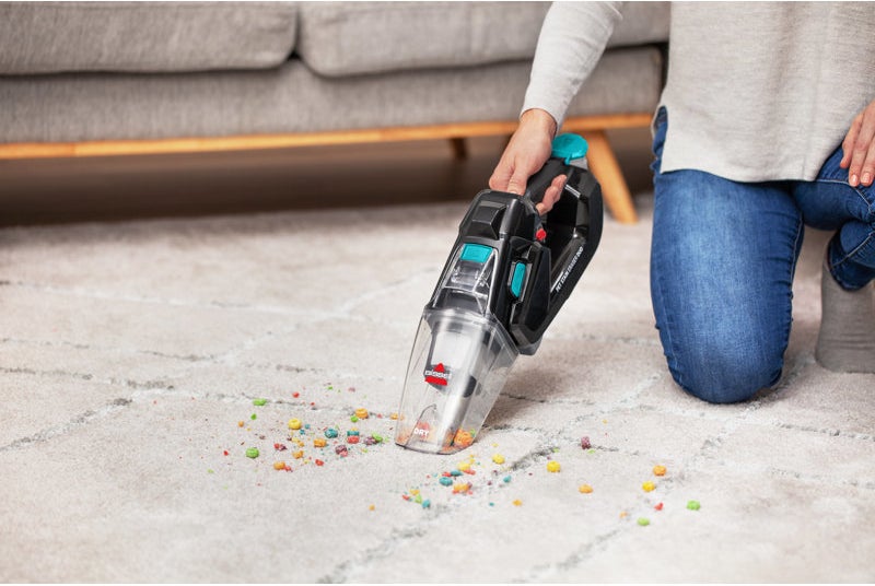 Person using a handheld vacuum to clean up scattered cereal on a carpet