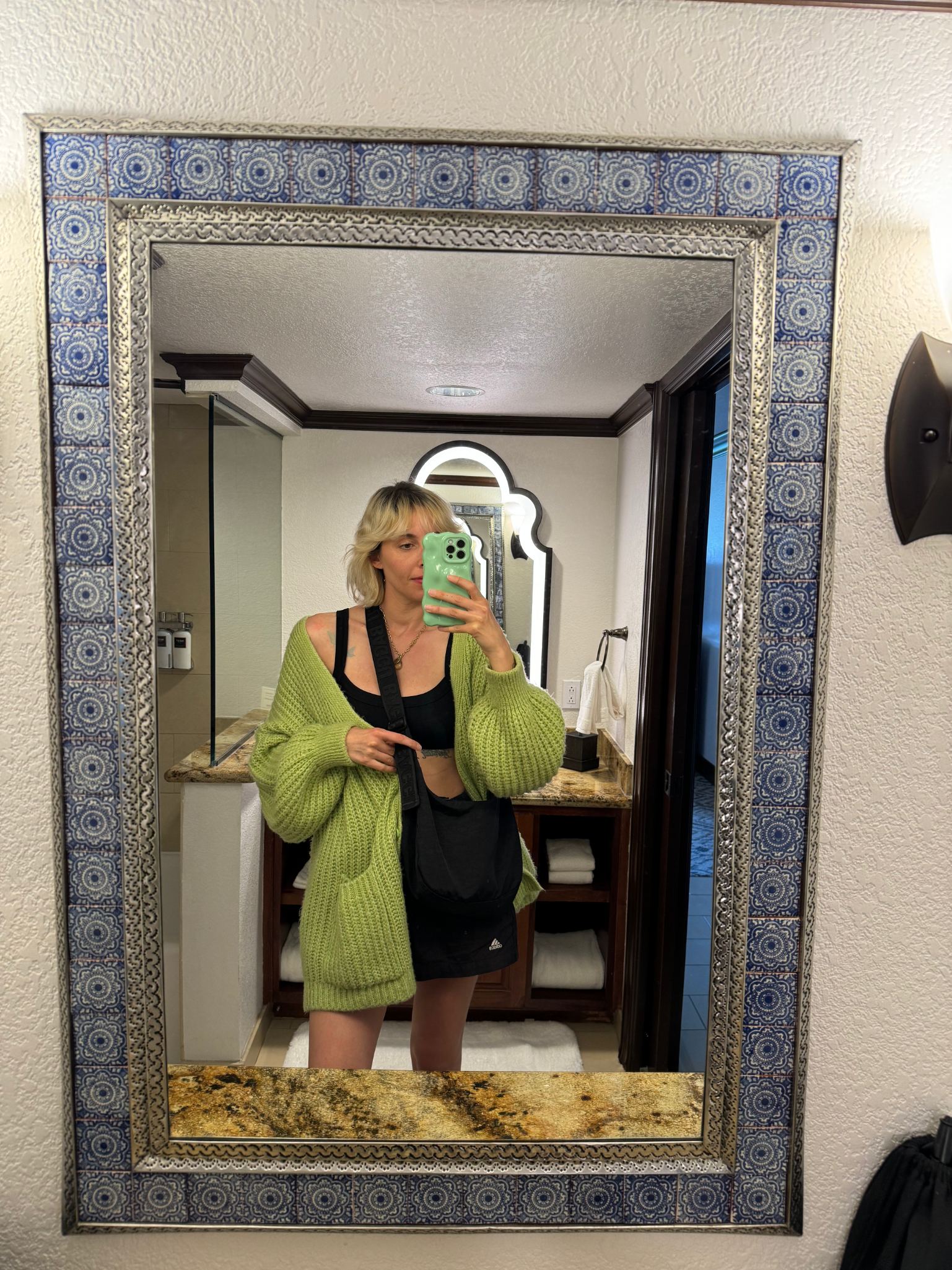 Person in a cozy sweater taking a mirror selfie in a hotel room