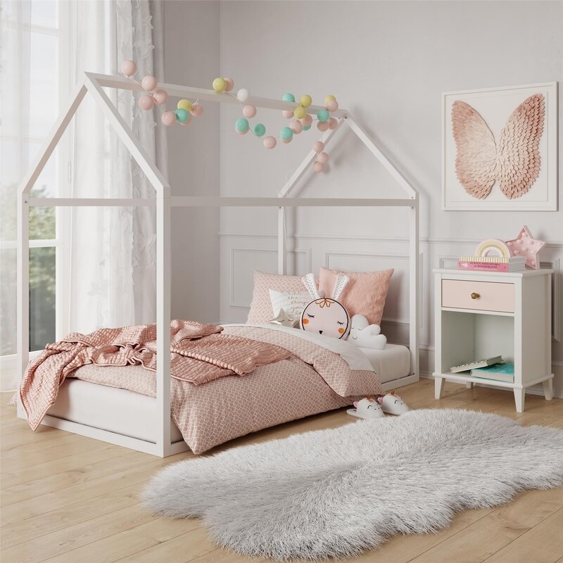 Child&#x27;s bedroom with a house-shaped bed frame, decorative pillows, and a side table