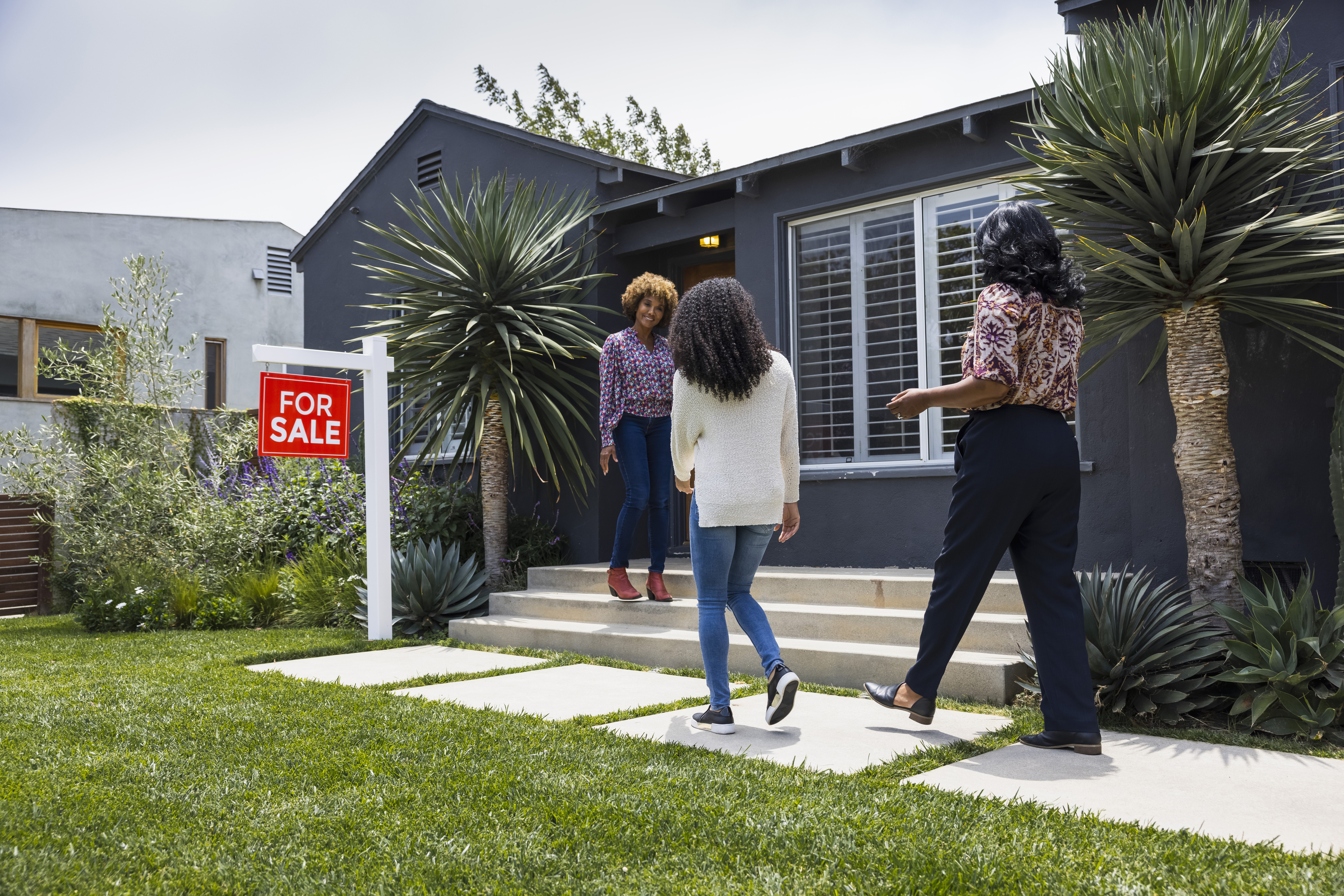 Three individuals exploring the exterior of a home with a &quot;For Sale&quot; sign