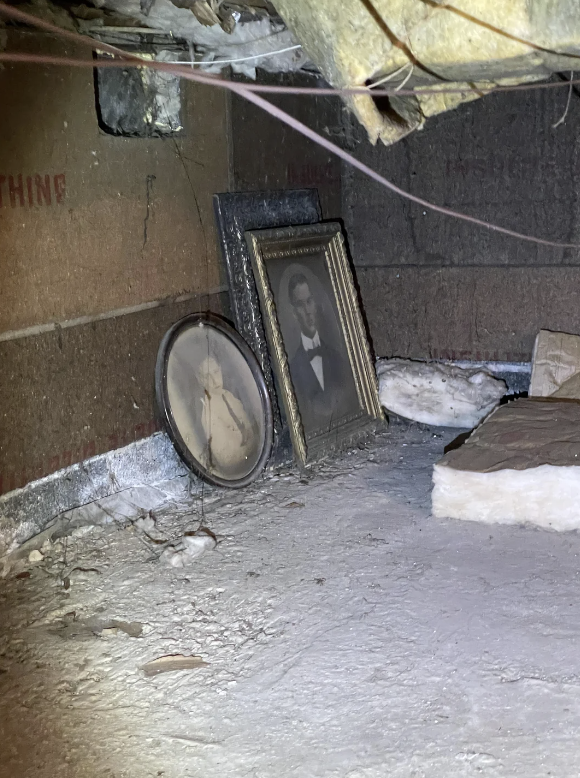 Two vintage framed portraits leaning against a wall in a dusty attic