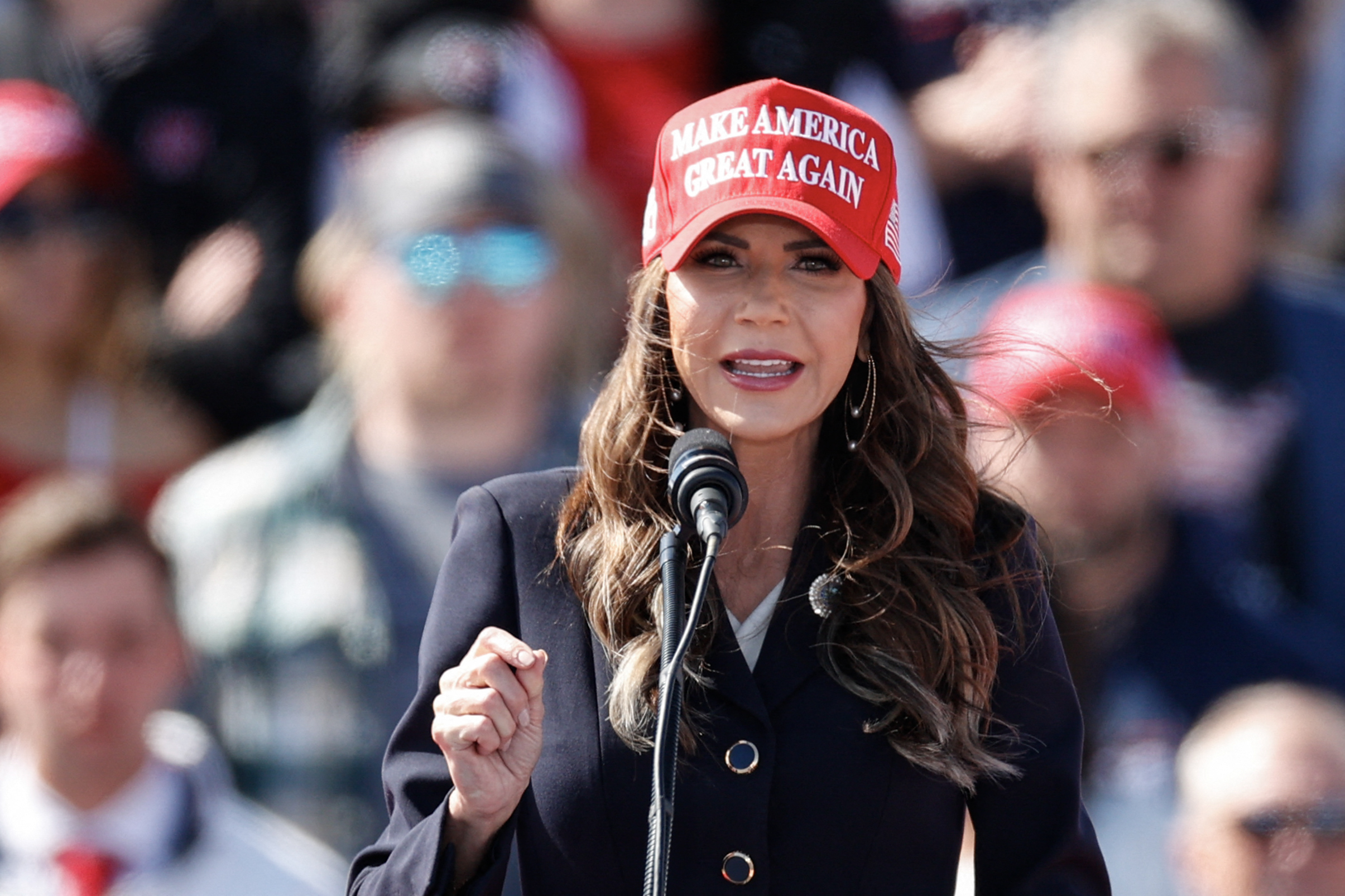 Woman speaking at a podium wearing a &quot;Make America Great Again&quot; hat
