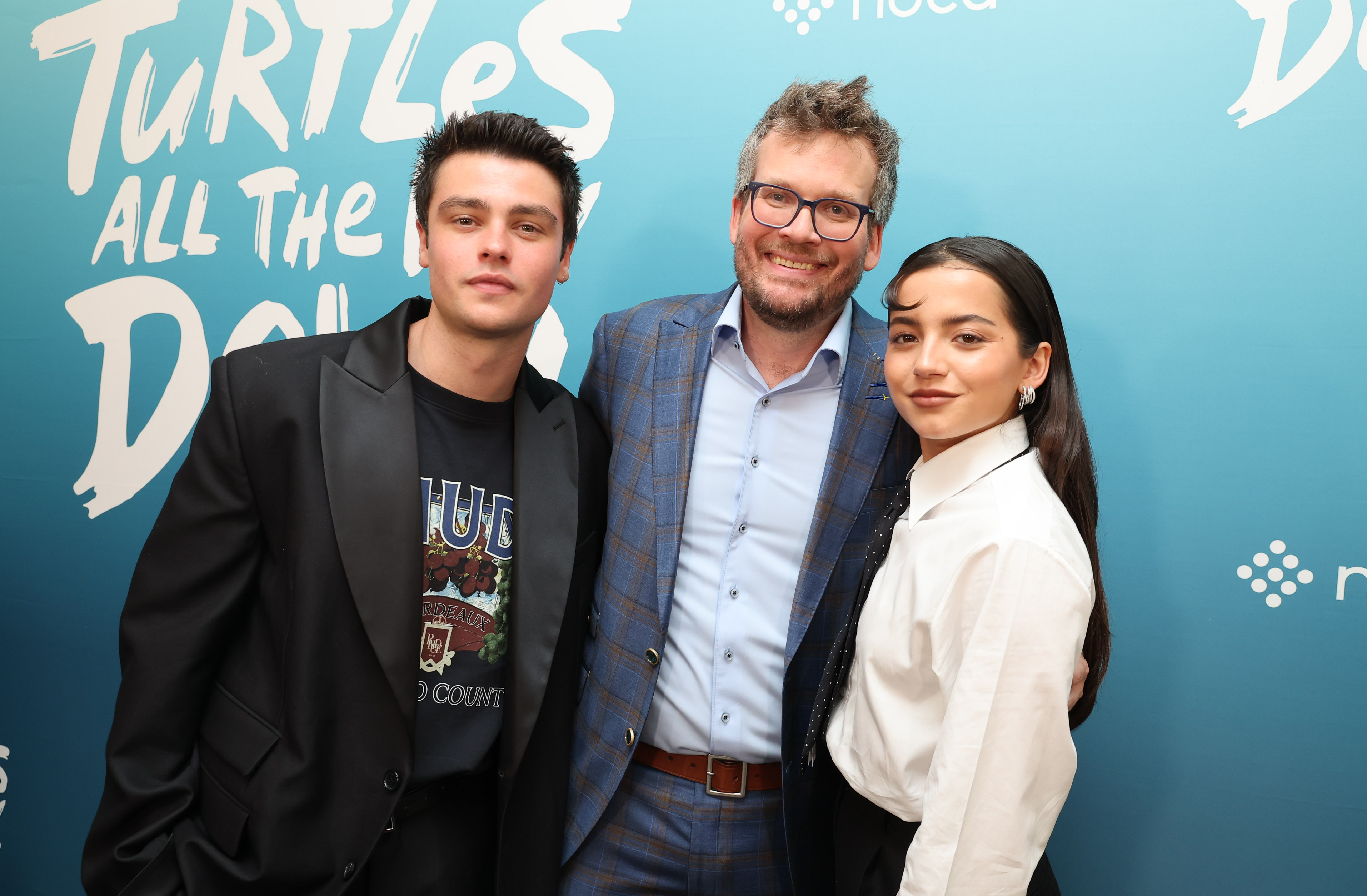 Three people posing at an event, flanked by a backdrop with text and a turtle graphic