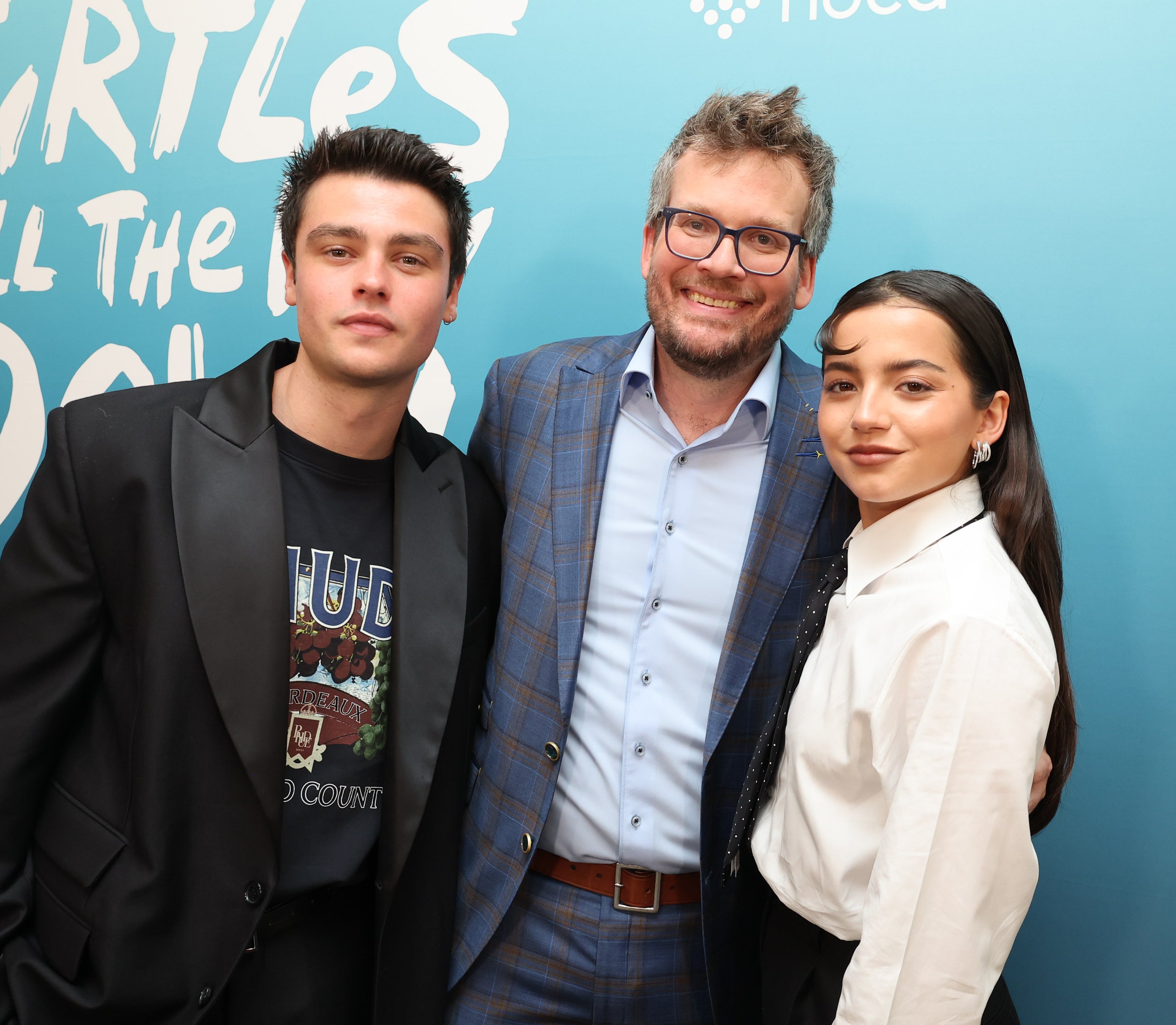 Three people posing at an event, flanked by a backdrop with text and a turtle graphic