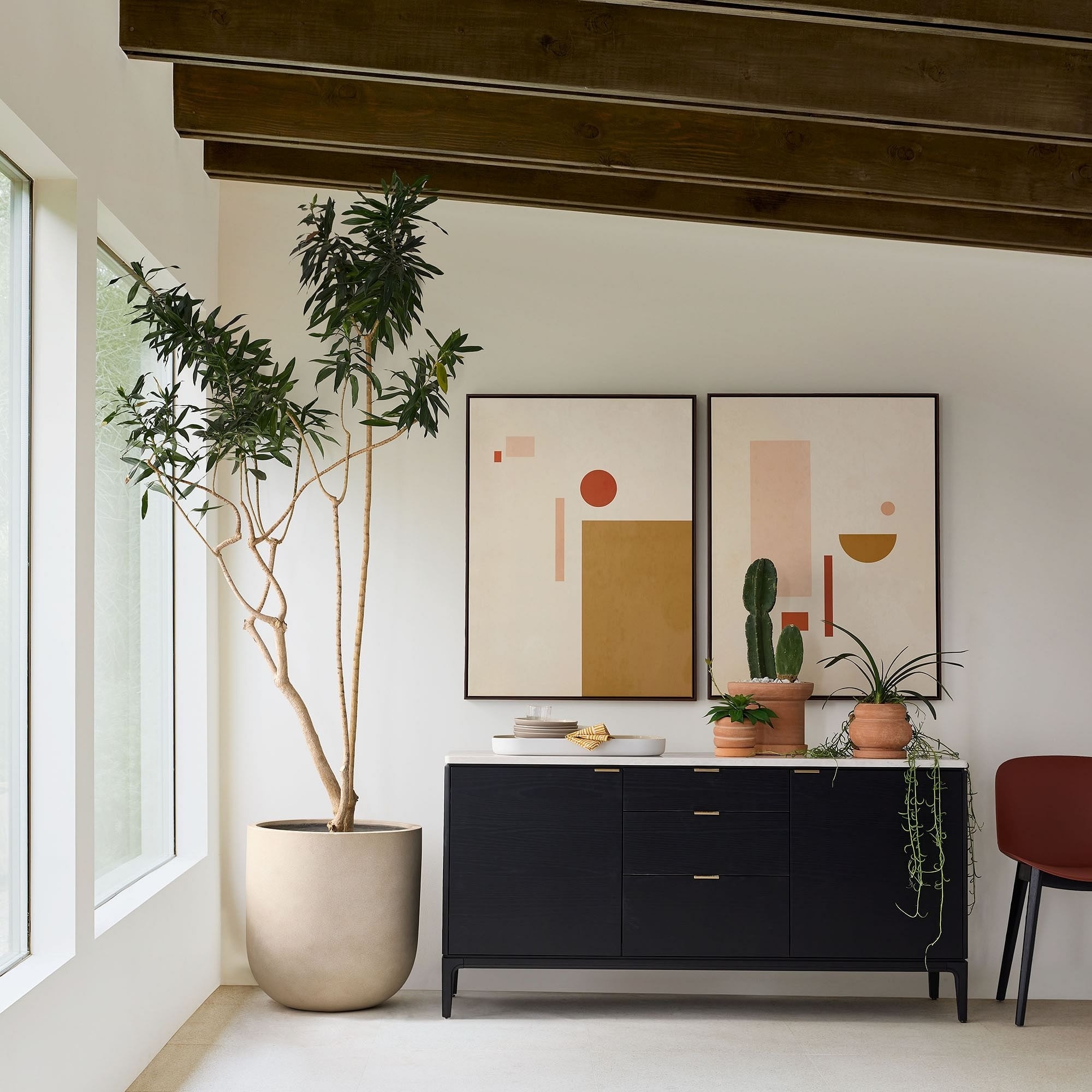 A minimalist room with a sleek sideboard, two abstract paintings, a potted plant, and decor items, evoking a modern aesthetic for shopping inspiration