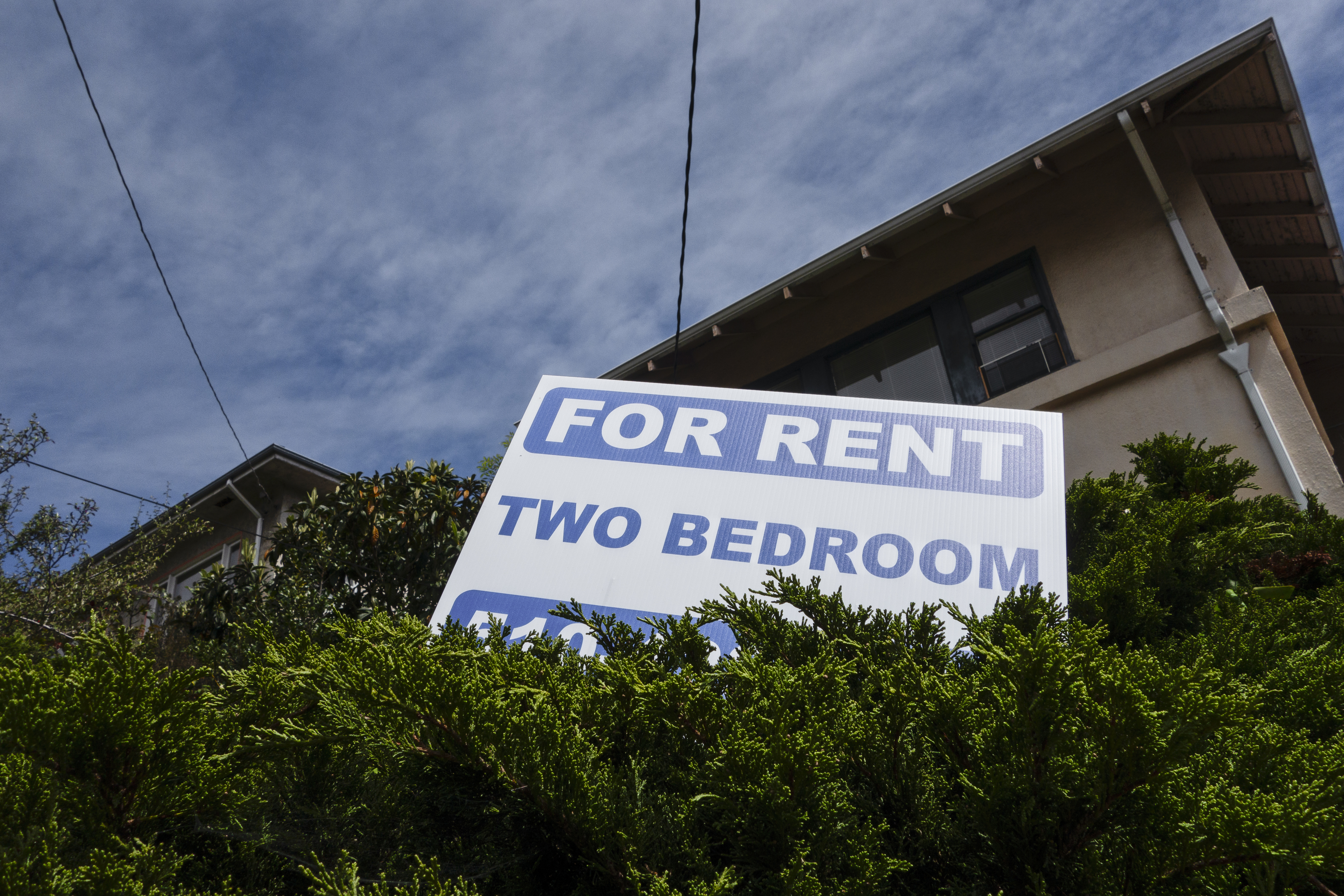 Sign reads &quot;FOR RENT TWO BEDROOM&quot; in front of a residential building with greenery