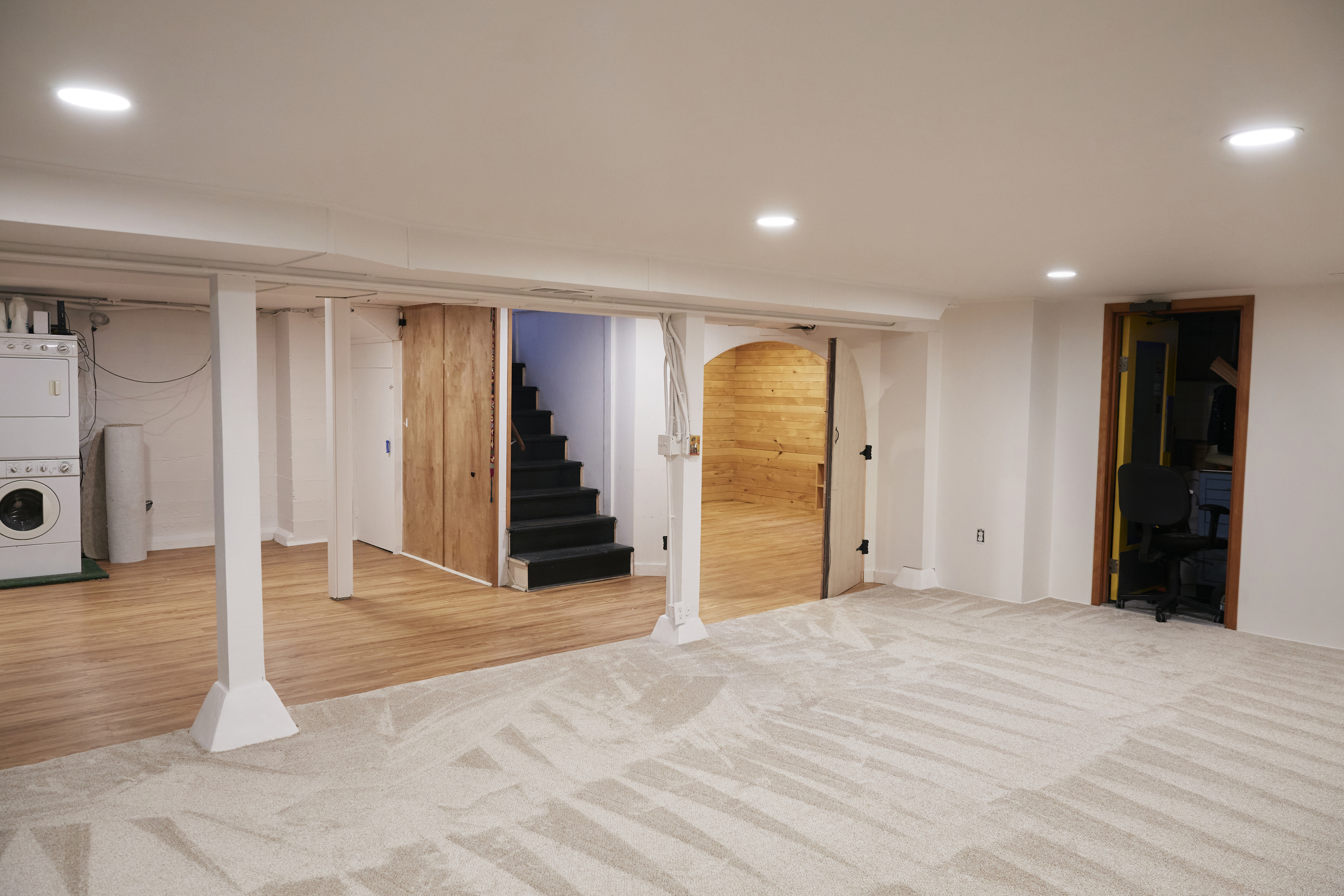 Basement interior with carpeted floors, white columns, laundry appliances, and a wooden staircase