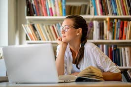 Woman at desk with laptop and book, looking thoughtful