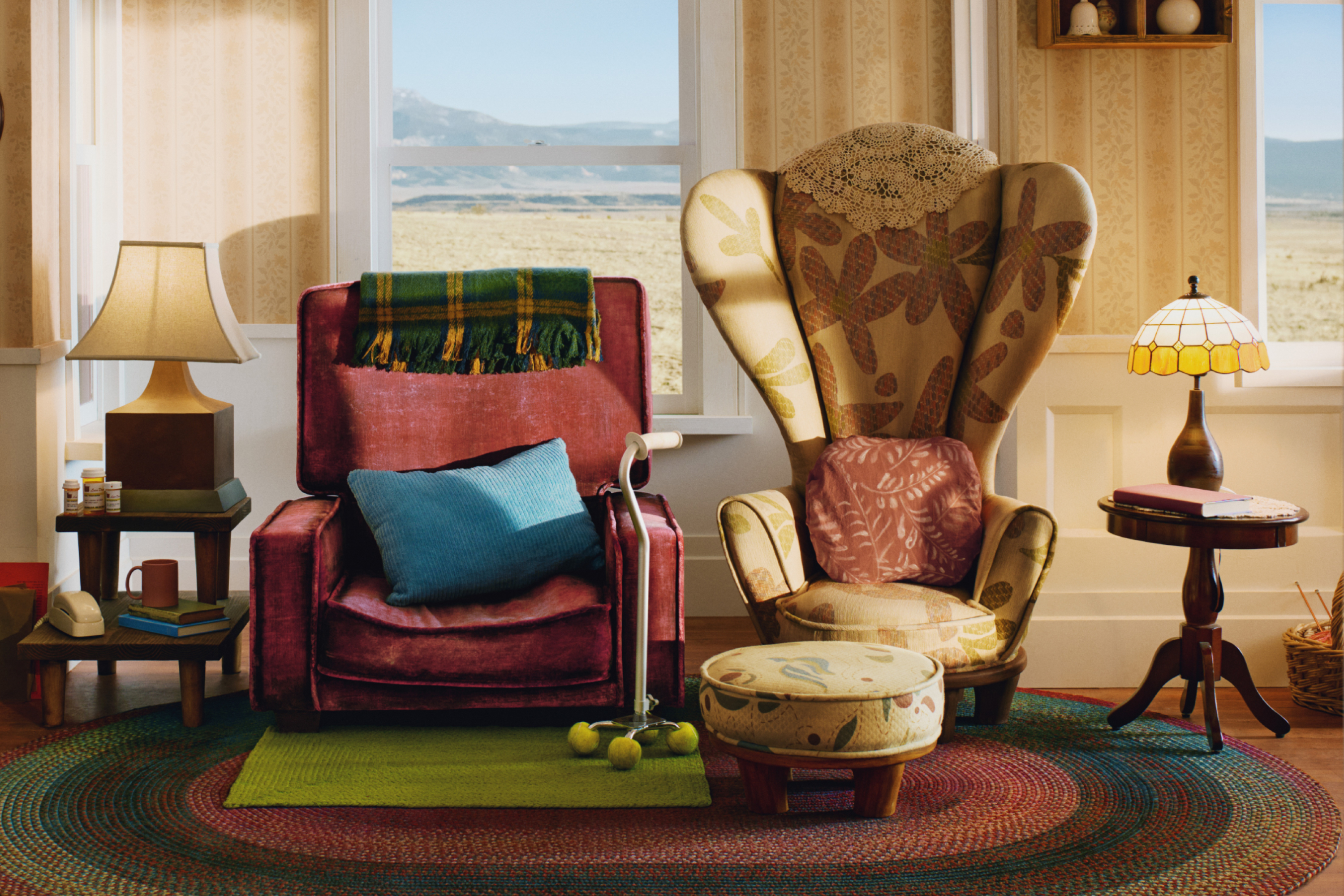 Cozy living room corner with a plush chair, patterned ottoman, rugs, and vintage lamps by a window