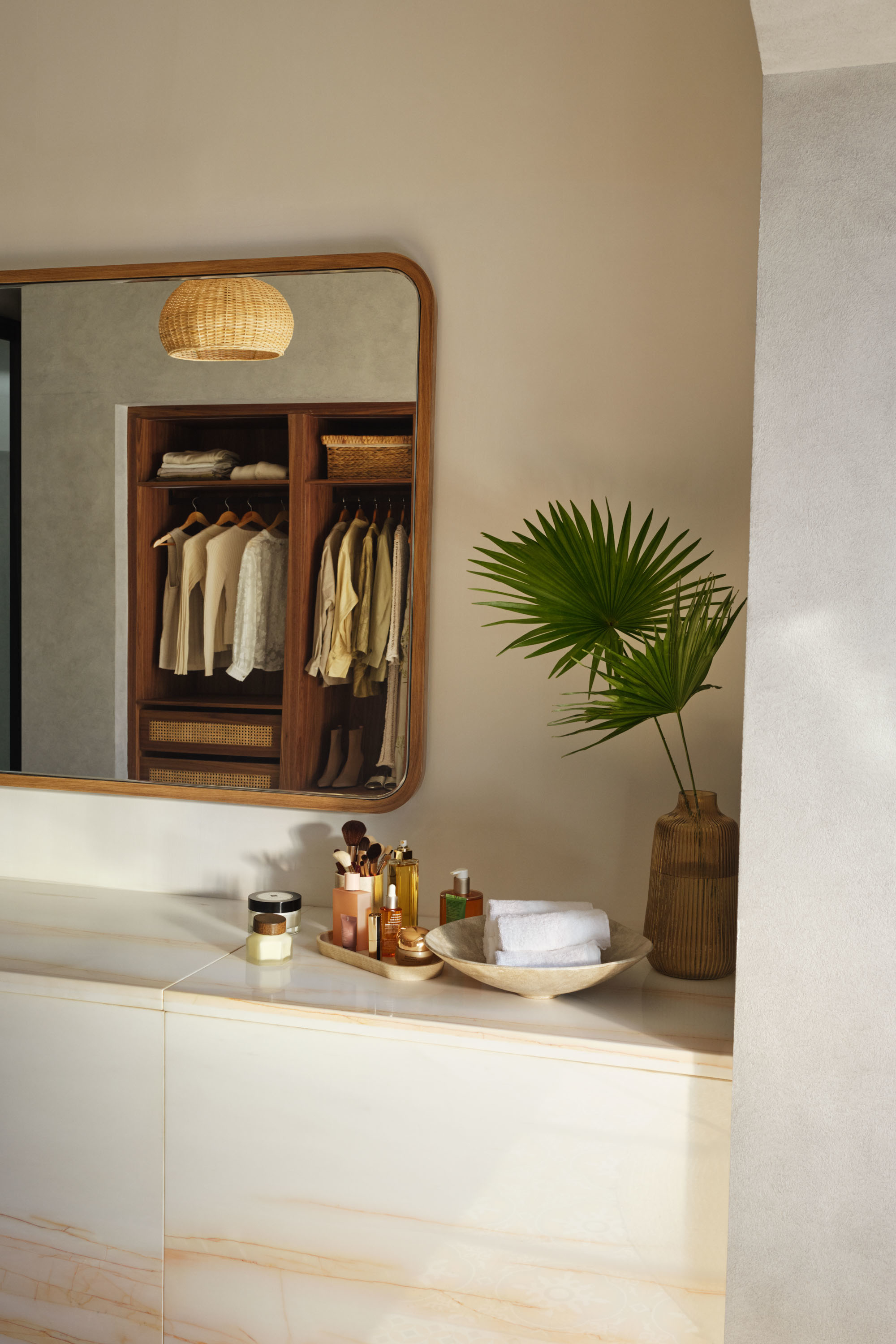 A bathroom vanity with a mirror above, showcasing neatly organized toiletries and towels, adjacent to a plant