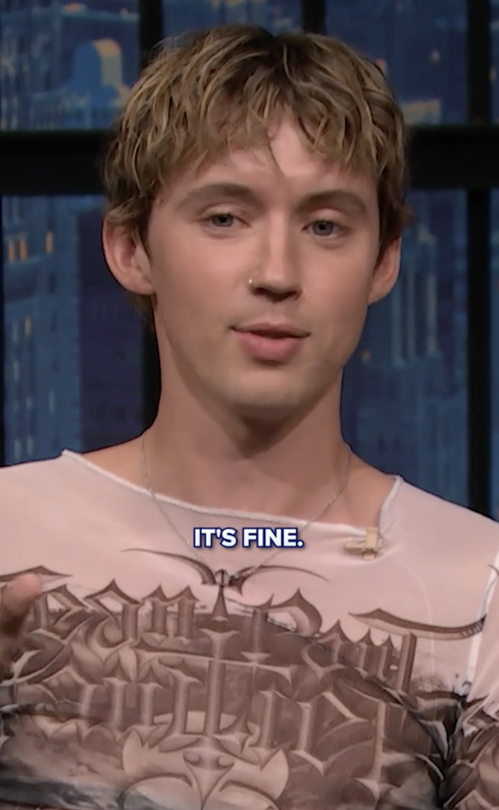 Male celebrity wearing a graphic shirt on a talk show, subtitle reads &quot;IT&#x27;S FINE.&quot;