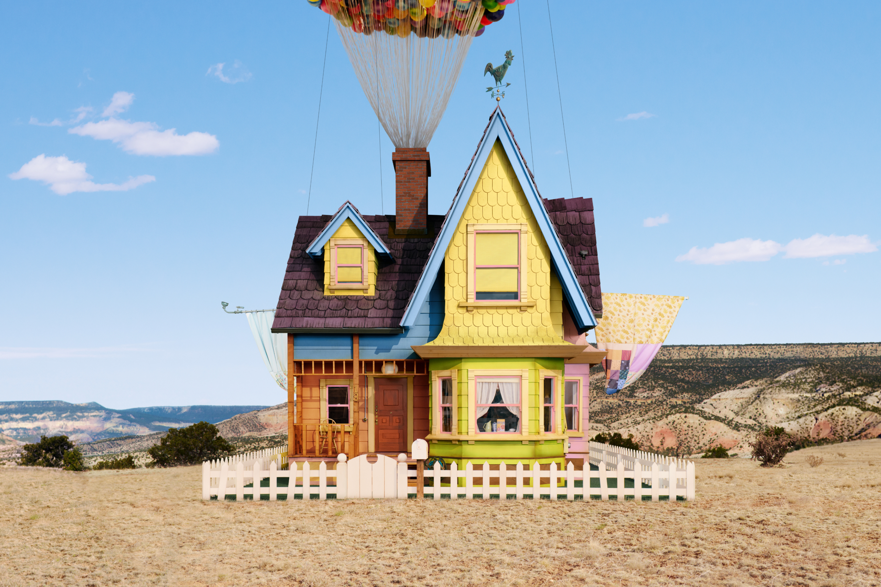 House floating with balloons over landscape, resembling scene from animated film 'Up'