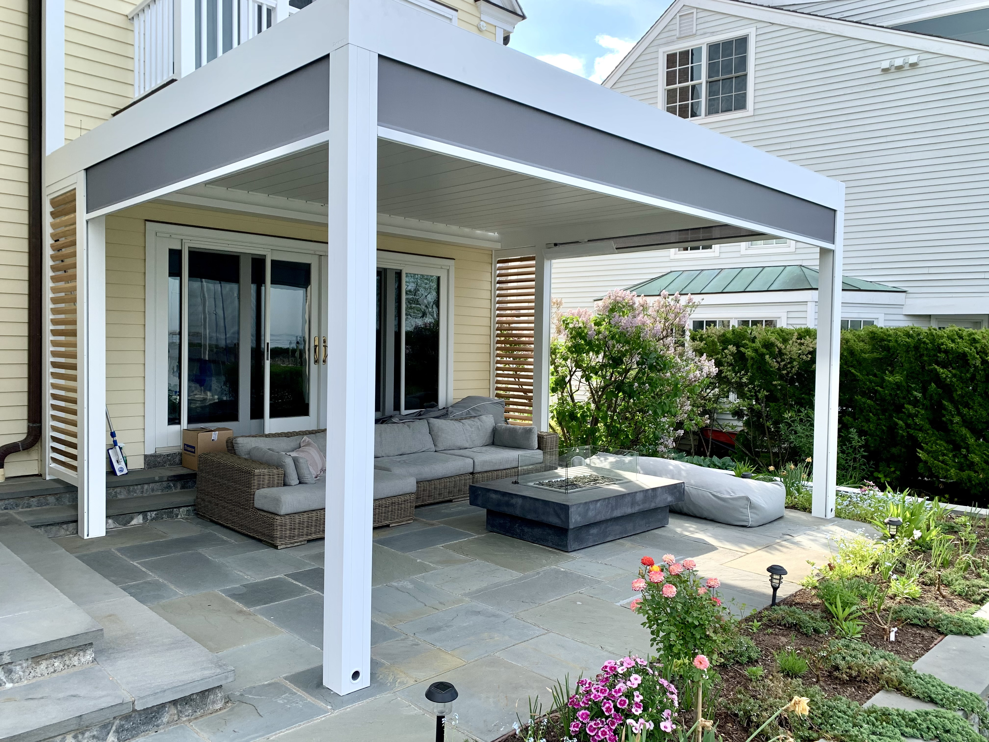Home exterior with patio seating under a pergola, adjacent to a garden