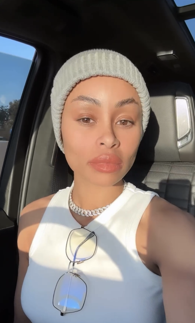 Blac Chyna in a car wearing a beanie and a tank top, accessorized with a chunky necklace and glasses
