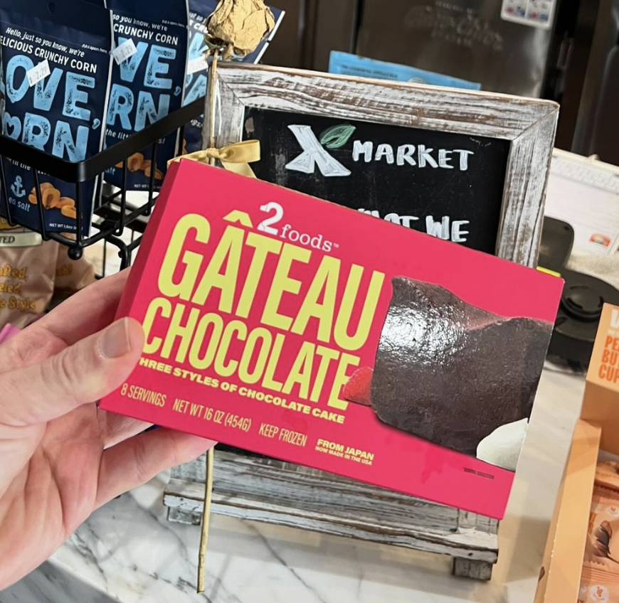 Hand holding a box of Gateau Chocolate in a market setting with other products in the background