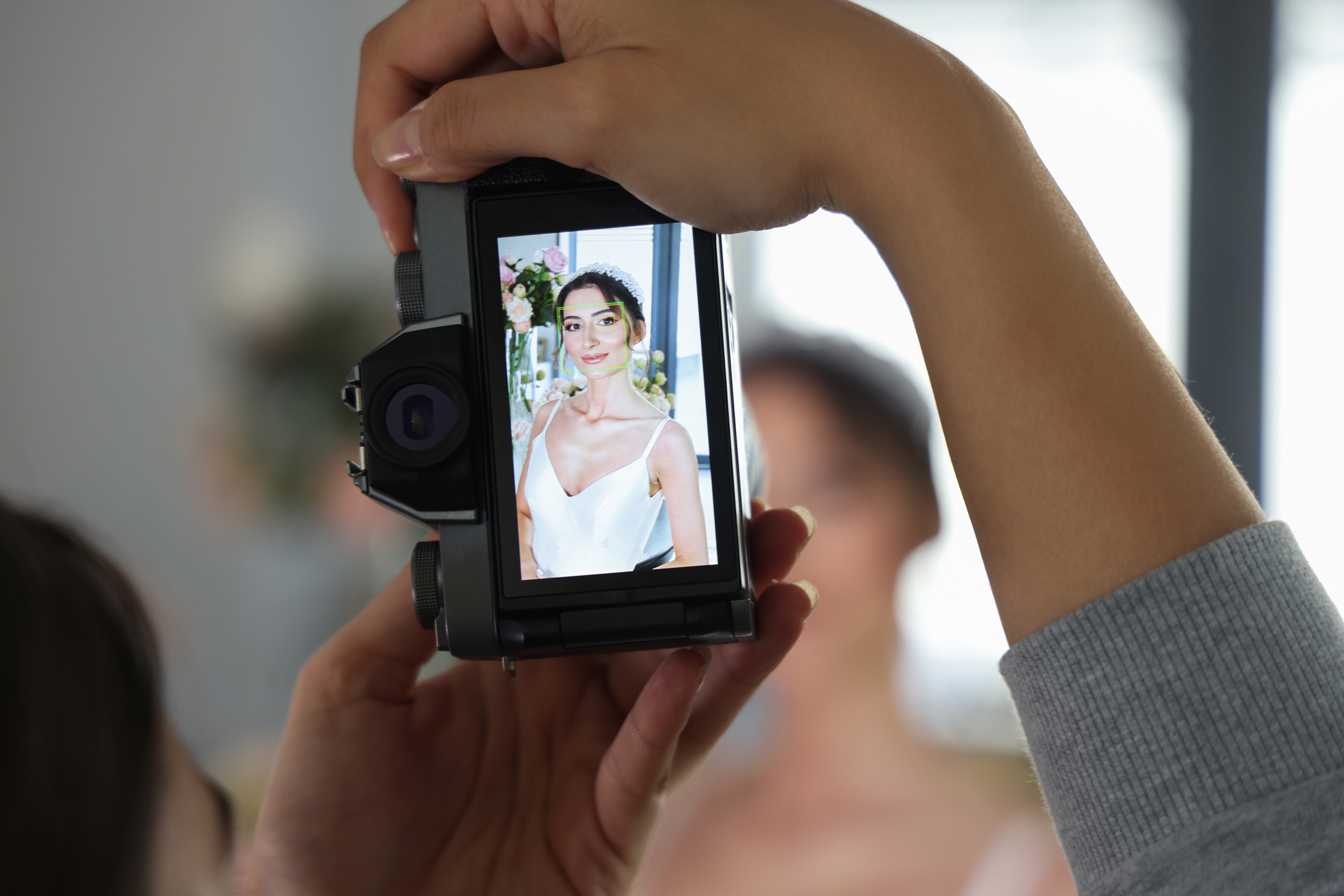 Bride in a white dress holding a bouquet, captured on a camera&#x27;s screen, others blurred in background