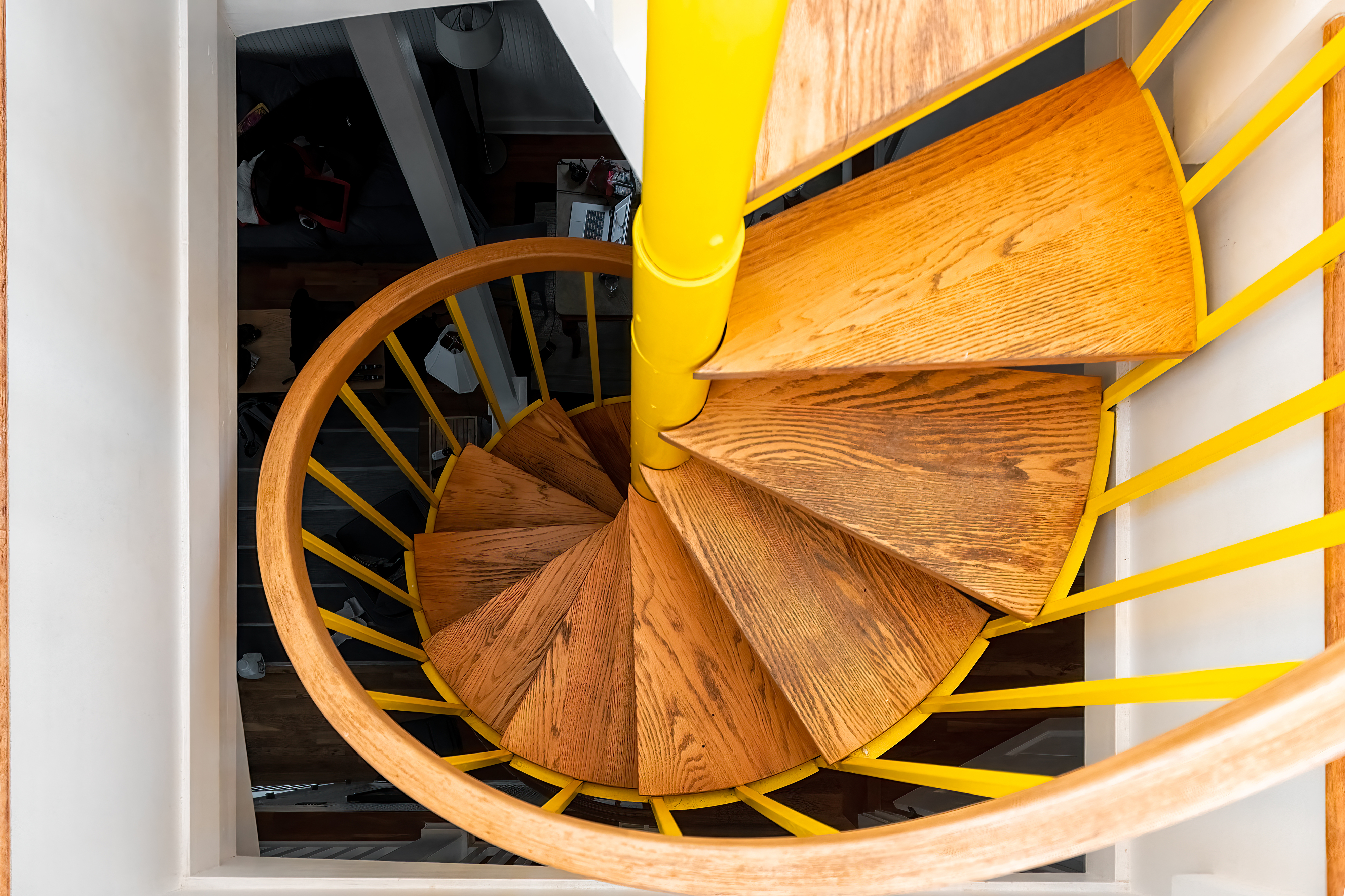 Spiral staircase with wooden steps and yellow central pole, viewed from above