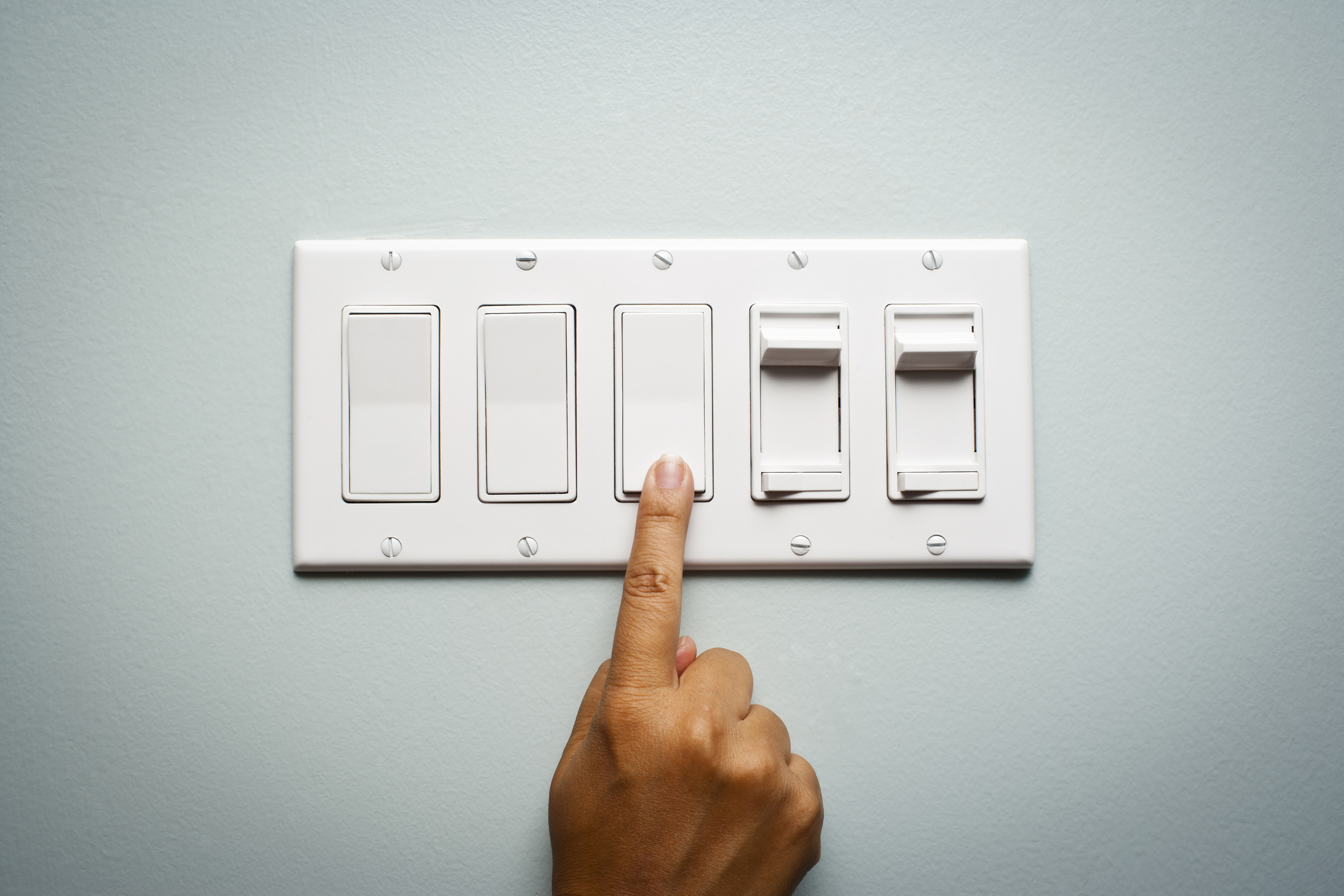 A hand is flipping one switch in a group of five on a wall