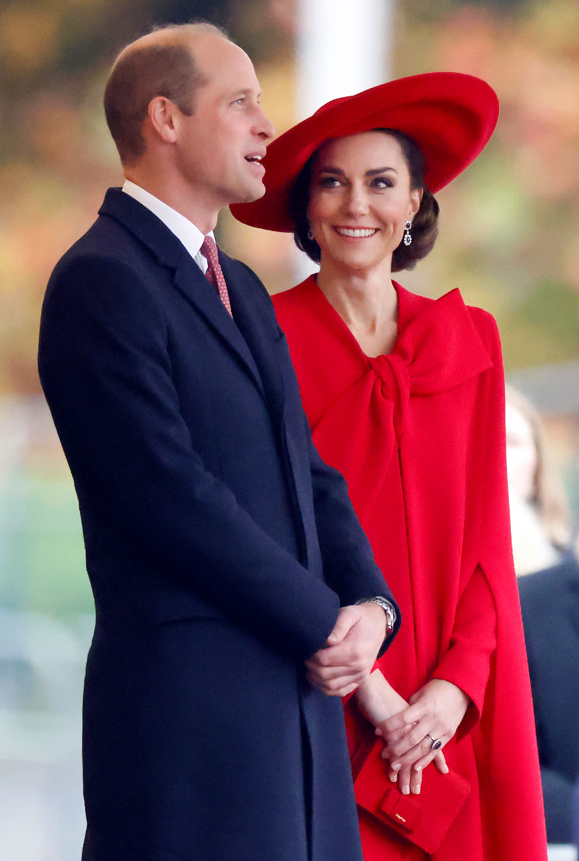 Prince William and Kate Middleton smiling, Kate in a red hat and matching coat with a bow