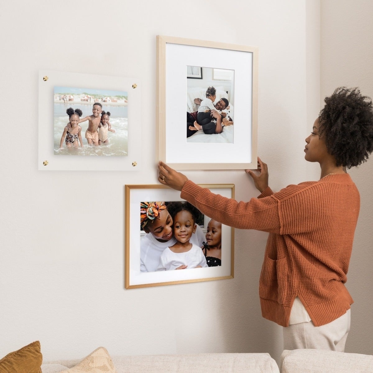 Person arranging three framed photos on a wall, featuring family moments for interior decoration