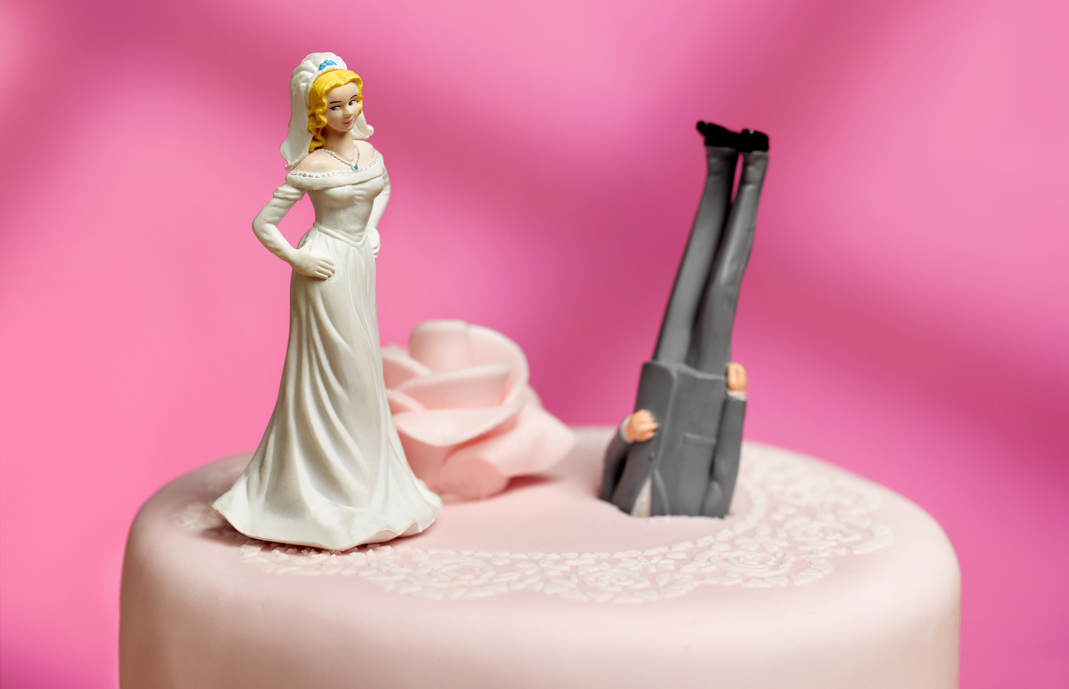 Bride figurine on cake with groom figurine legs upside down, indicating playful wedding cake topper