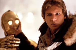 Harrison Ford as Han Solo, in a vest and parka, next to C-3PO from Star Wars putting his hand over C-3PO's mouth.