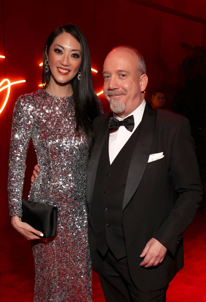 Two individuals posing together, one in a sparkling dress and clutch, the other in a tuxedo with a bow tie