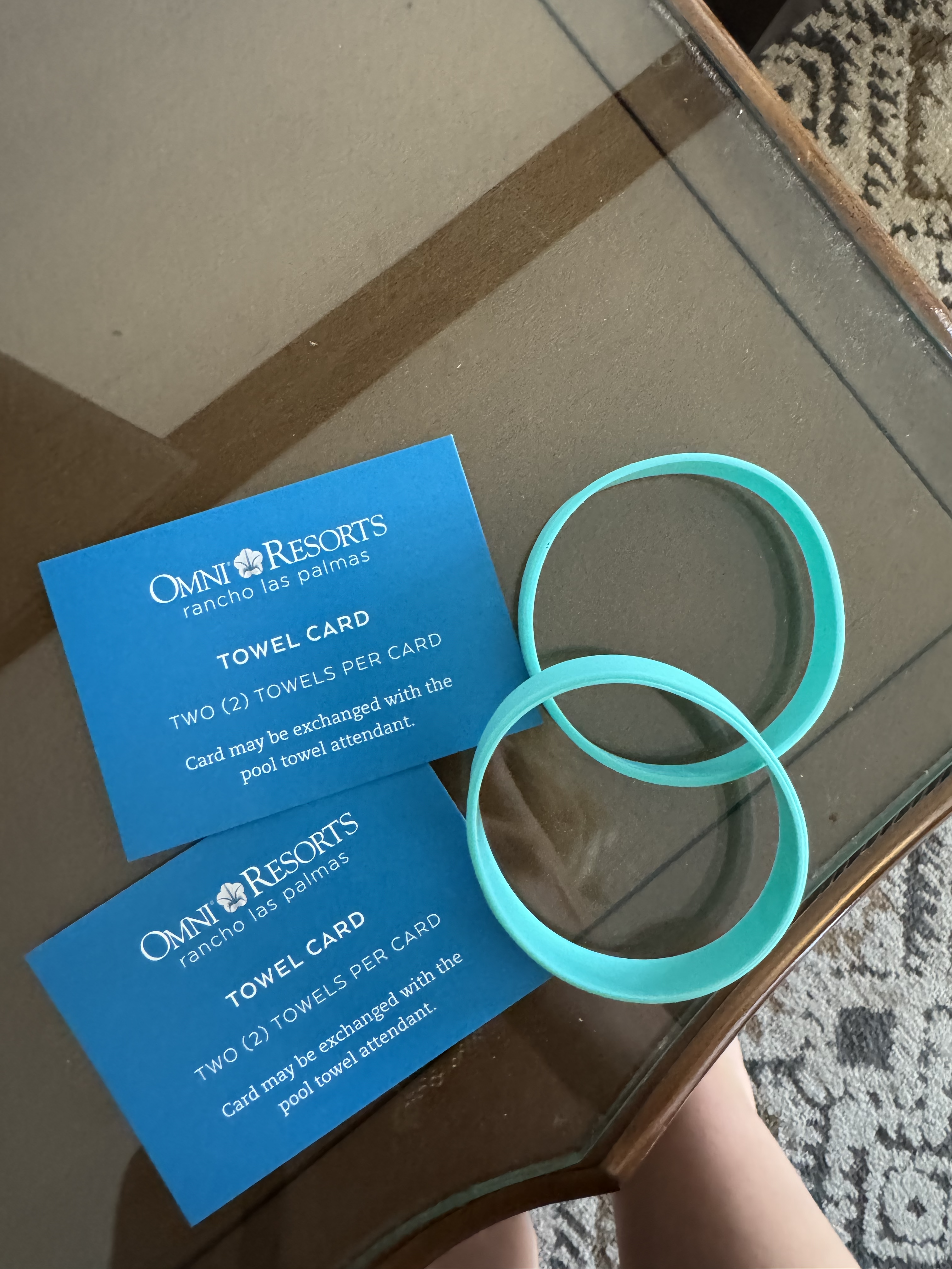 Two blue cards on a surface with text about towel exchange policy at Omni Resorts, accompanied by two teal wristbands