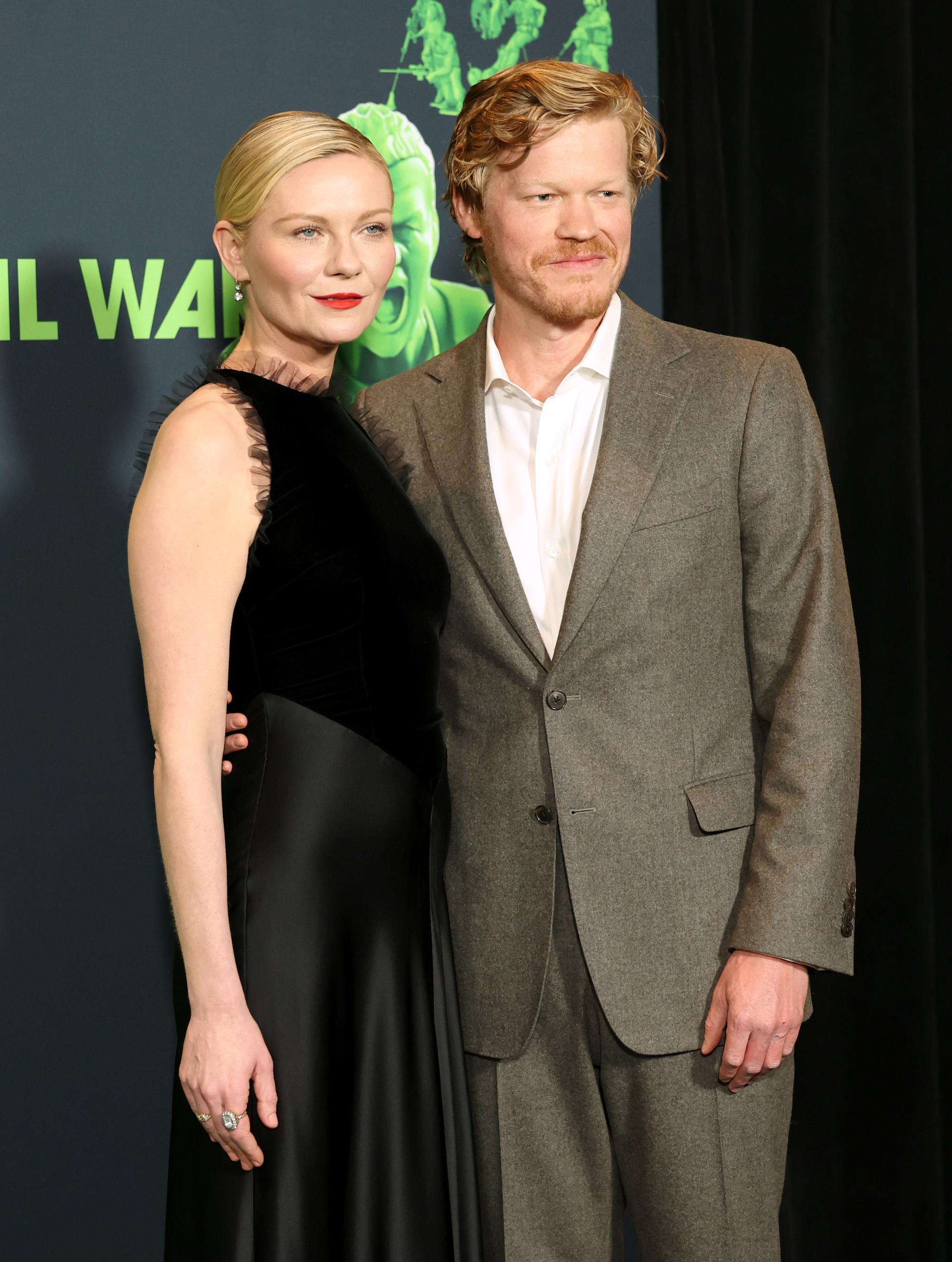 Two actors posing together; one in a black sleeveless dress, the other in a grey suit with a white shirt