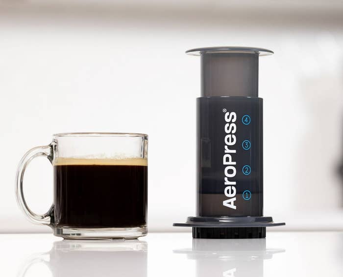 AeroPress coffee maker beside a glass cup of coffee on a countertop