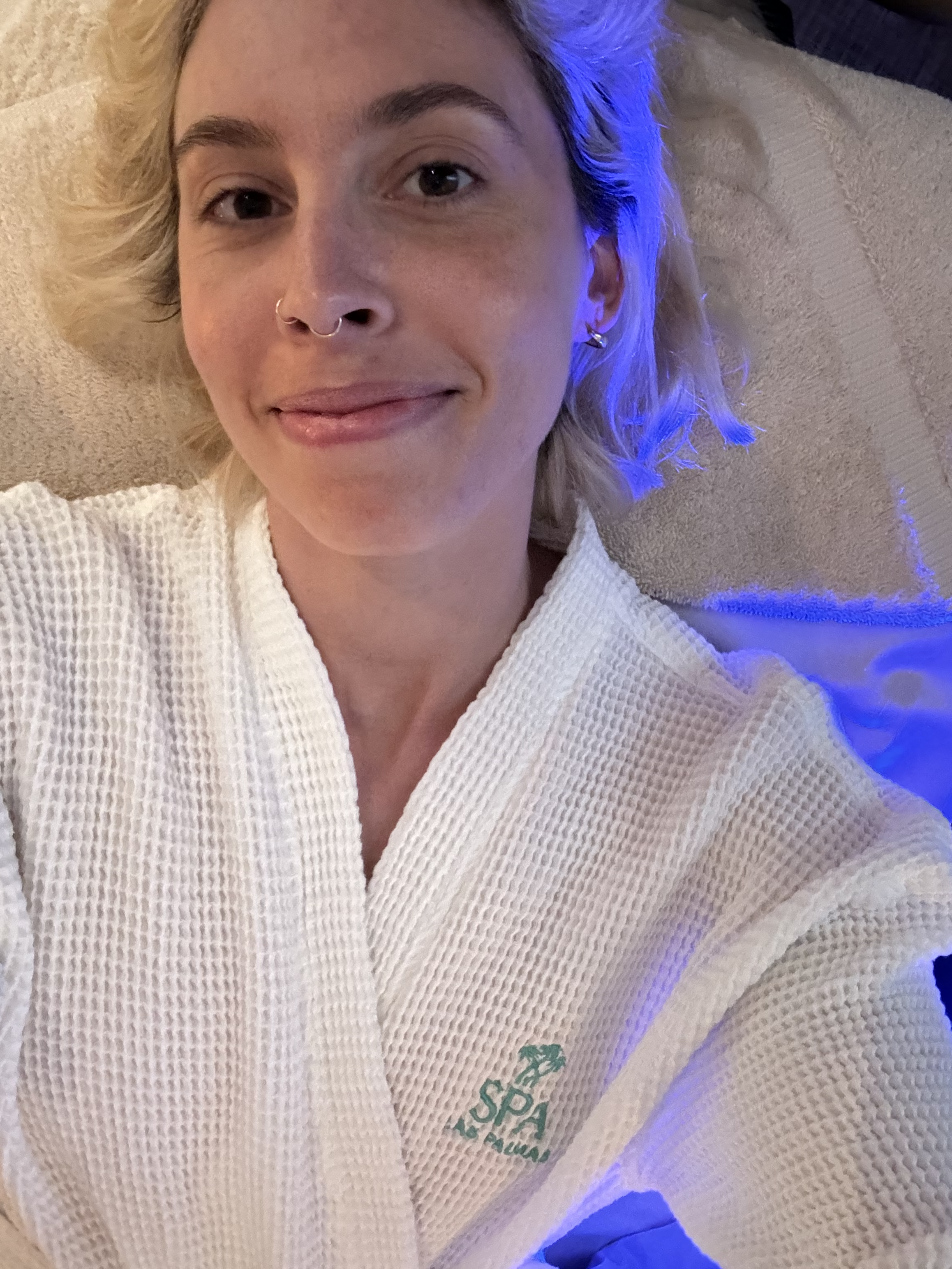 Woman in a spa robe smiling at the camera, likely enjoying a relaxing experience at a travel destination spa